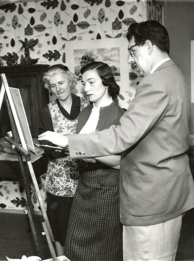 Old photo of student being instructed on a painting from professors